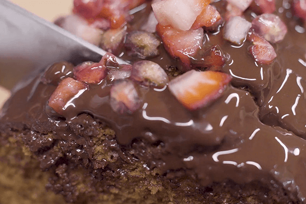 Knife chopping chocolate sponge cake covered with melted chocolate decorated with pomegranate